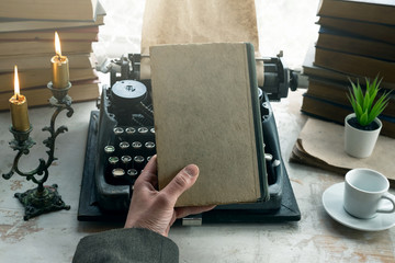 A writer is holding in hands a closed book with blank cover for copy space on a table background.