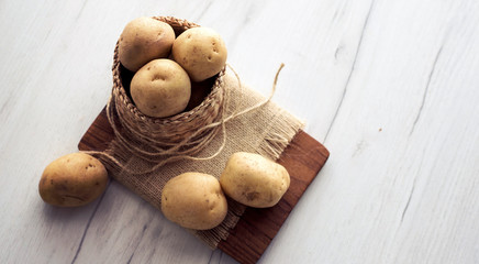 Raw potatoes in rustic wooden plate, on bright background. Organic agriculture & food concept.