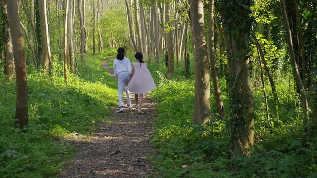 Two little girls holding hands and skipping together on a forest path, in slow motion 