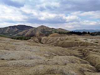Arid landscape created by the Mud Volcanoes in Berca, Romania. A mud volcano or mud dome is a landform created by the eruption of mud or slurries, water and gases