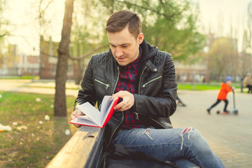 Obraz premium Man with a notebook in his hands in the Park. Male, student is writing her ideas and thoughts into the notebook sitting on the bench in the park