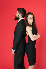 Man bearded hipster and woman in formal dress red background. Formal fashion and elegant clothes. Luxury fashion boutique. Fashion clothes shop. Official event. Couple man in tuxedo and elegant girl