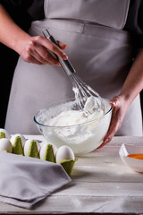 young woman in a gray aprons breaks the eggs