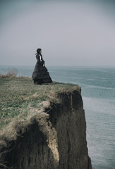Outdoors portrait of a victorian lady in black standing on the cliff.