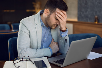 Mid adult businessman having headache while working on laptop in a cafe