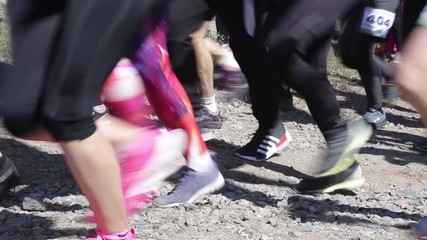 Crowd of amateur athletes running marathon cross country. Many human legs close up.