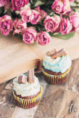 Handmade chocolate muffins with decorations. Book and a bouquet of roses, blurred background