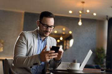 Mid adult businessman surfing the internet on his smart phone in a cafe
