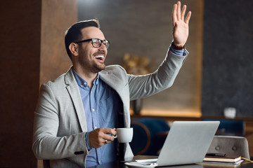 Businessman enjoying coffee and waving to someone