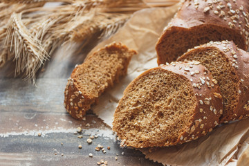Handmade bread with bran and ears of wheat, wooden background