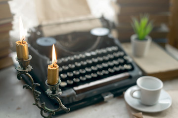 Typewriter, stack of books, candle and a empty cup of coffee or tea on a writer table background.