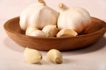Garlic Cloves and Bulb in vintage wooden plate on white wooden table.