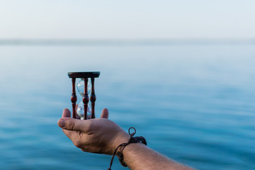 Hourglass in male hand on the background of the sea.