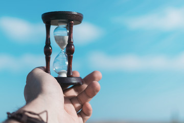 Hourglass in male hand on the background of the sky.