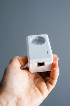 Man hand holding against gray background a new powerline Ethernet internet adapter  showing the rear part with the RJ-45 plug pair button