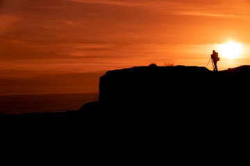 Silhouette of a photographer who shoots a sunset, on top of castle at sunset background.