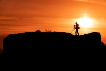 Silhouette of a photographer who shoots a sunset, on top of castle at sunset background.