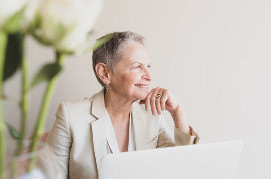 Closeup Of Beautiful Senior Professional Woman Resting Head On Hand At Desk With Computer And Flowers - Selective Focus