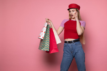 Young beautiful shocked girl in red hat with colorful shopping bags