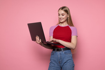 Happy smiling cheerful female with blond hair, wearing casual clothes, holding laptop in hand