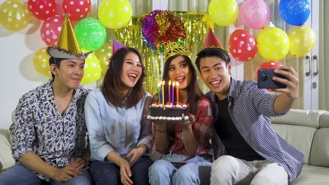 Group of cheerful young people taking selfie photo with a mobile phone while celebrating their friend birthday at home. Shot in 4k resolution