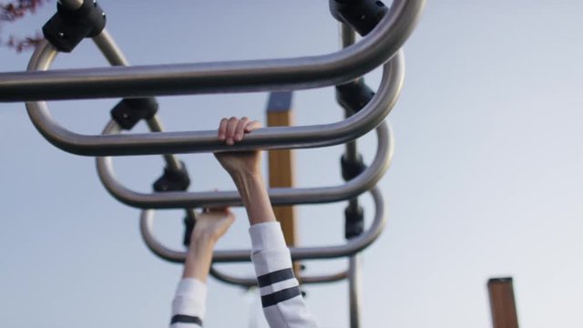 Young girl making her way across monkey bars in a park, in slow motion