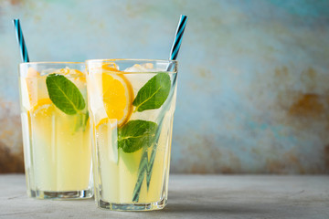 Two glass with lemonade or mojito cocktail with lemon and mint, cold refreshing drink or beverage with ice on rustic blue background. Copy space