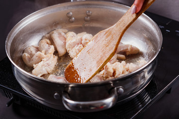young woman in a gray aprons roasts chicken fillet with carrots