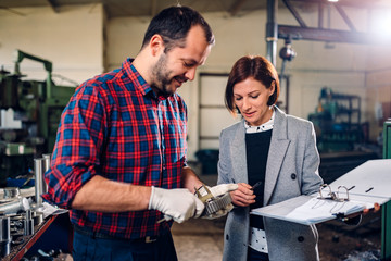 Machinist standing with female engineer and measuring cogwheel diameter