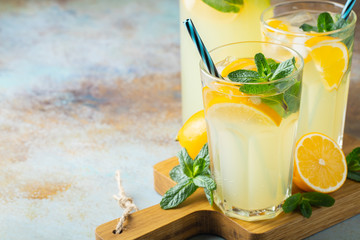 Two glass with lemonade or mojito cocktail with lemon and mint, cold refreshing drink or beverage with ice on rustic blue background. Copy space