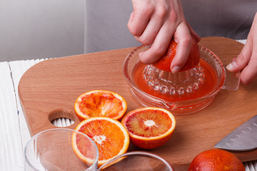 young woman in a gray apron squeezes juice of orange blood