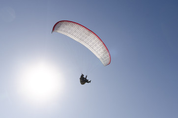 A man flies on a paraglider over green fields in the hot summer. Against the background of blue sky and rare clouds