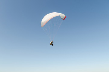 A man flies on a paraglider over green fields in the hot summer. Against the background of blue sky...