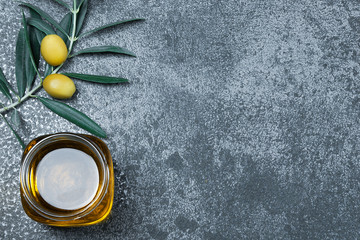 Glass jar of olive oil and olive tree branch, raw turkish olive seeds and leaves on grey rustic vintage table. Olives background olivae oleum