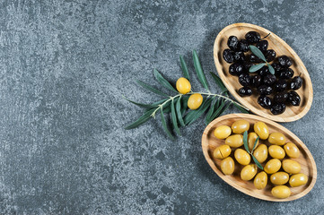 Black and green olives in bamboo bowl with olive tree branch ,raw turkish olive seeds and leaves on grey rustic vintage table. Olives background olivae oleum