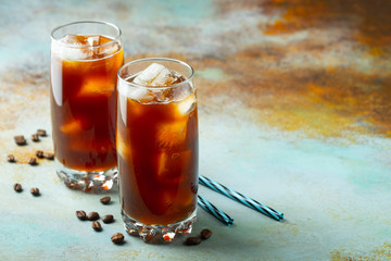 Ice coffee in a tall glass with cream poured over and coffee beans. Cold summer drink on a blue rusty background with copy space