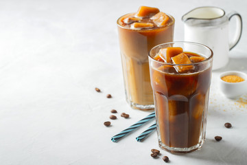 Ice coffee in a tall glass with cream poured over and coffee beans. Cold summer drink on a light background. With copy space