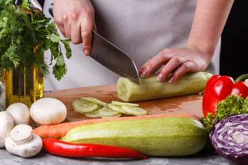 young woman in a gray apron cuts a cucumber