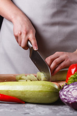 young woman in a gray apron cuts a cucumber