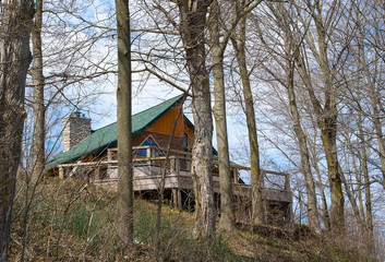 rustic cabin with wooden deck and green roof on a hill in spring woods