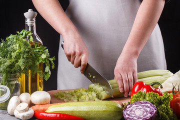 young woman in a gray apron cuts a celery