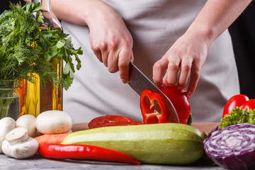 young woman slicing peppers in a gray apron