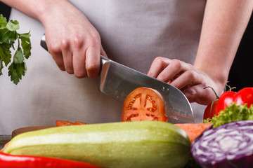 young woman slicing a tomato in a gray apron