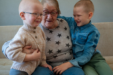 elderly woman sits and plays with her grandchildren on couch. Children love grandmother very much....