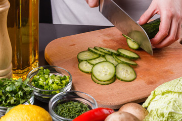 young woman in a gray apron cuts a cucumber