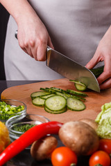 young woman in a gray apron cuts a cucumber