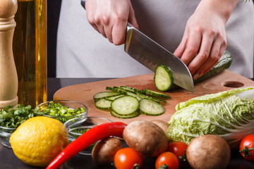 young woman in a gray apron cuts a cucumber