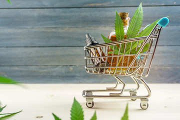 Supermarket trolley with marijuana leafs and medical cannabis oil cbd on wooden backdrop