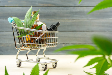 Supermarket trolley with marijuana leafs and medical cannabis oil cbd on wooden backdrop