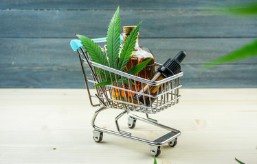 Supermarket trolley with marijuana leafs and medical cannabis oil cbd on wooden backdrop